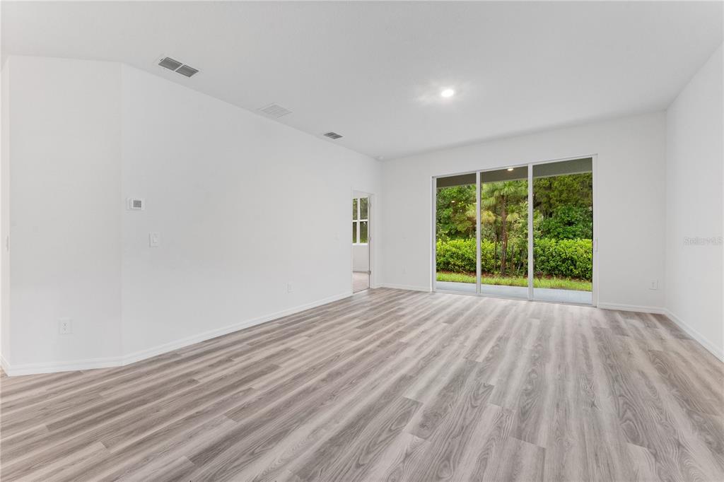 An empty room with light wood-look flooring, white walls, and sliding glass doors to greenery — 31351 PAPER BIRCH STREET, WESLEY CHAPEL, FL