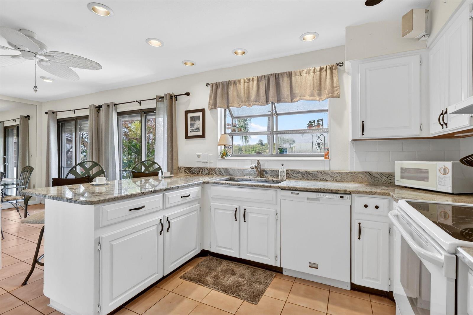 A kitchen with white cabinets, granite countertops, tile flooring, and a window over the sink — PORT ST. LUCIE, FL