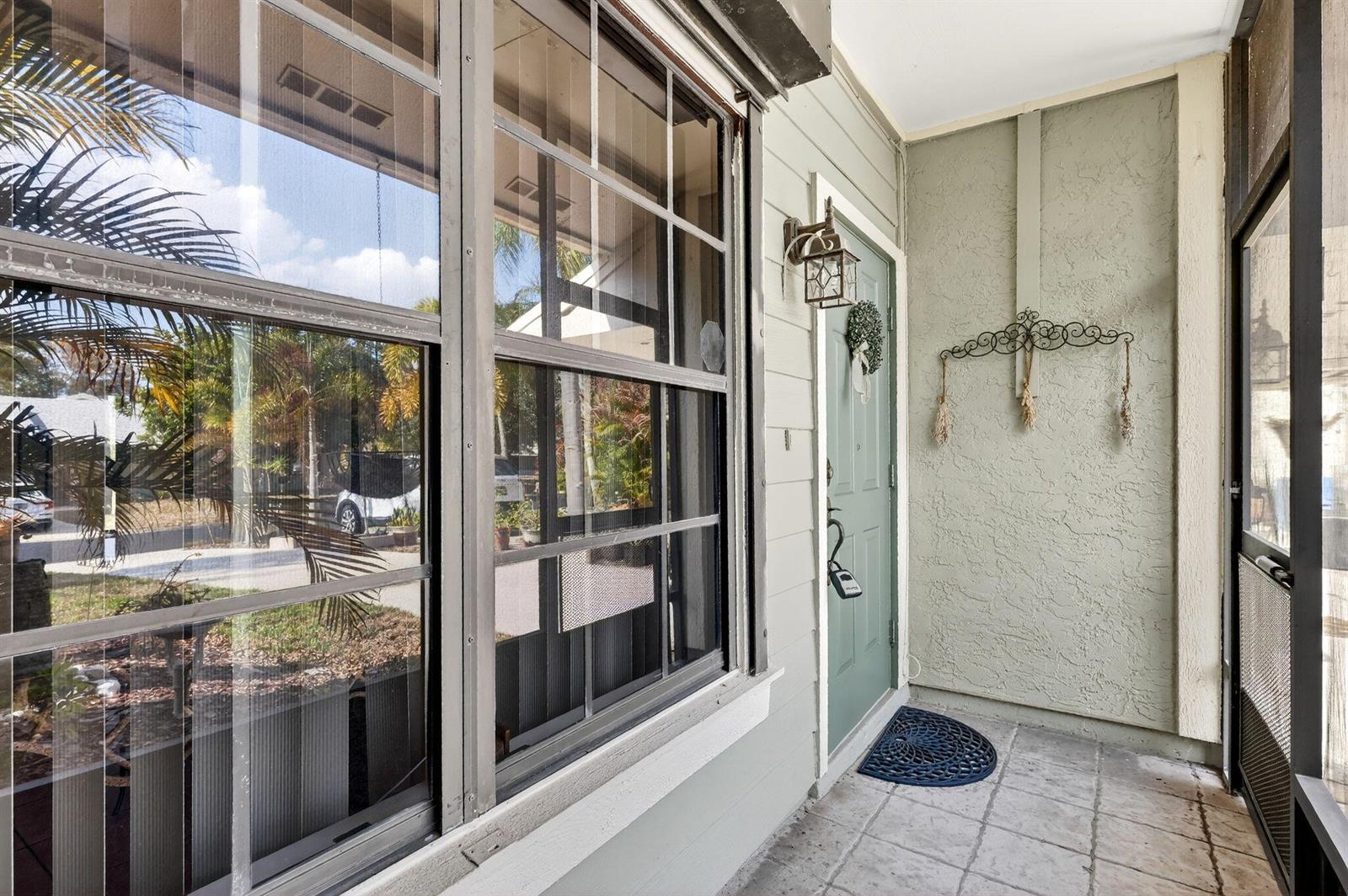 A covered porch features a green front door, a large window, and a tiled floor — PORT ST. LUCIE, FL