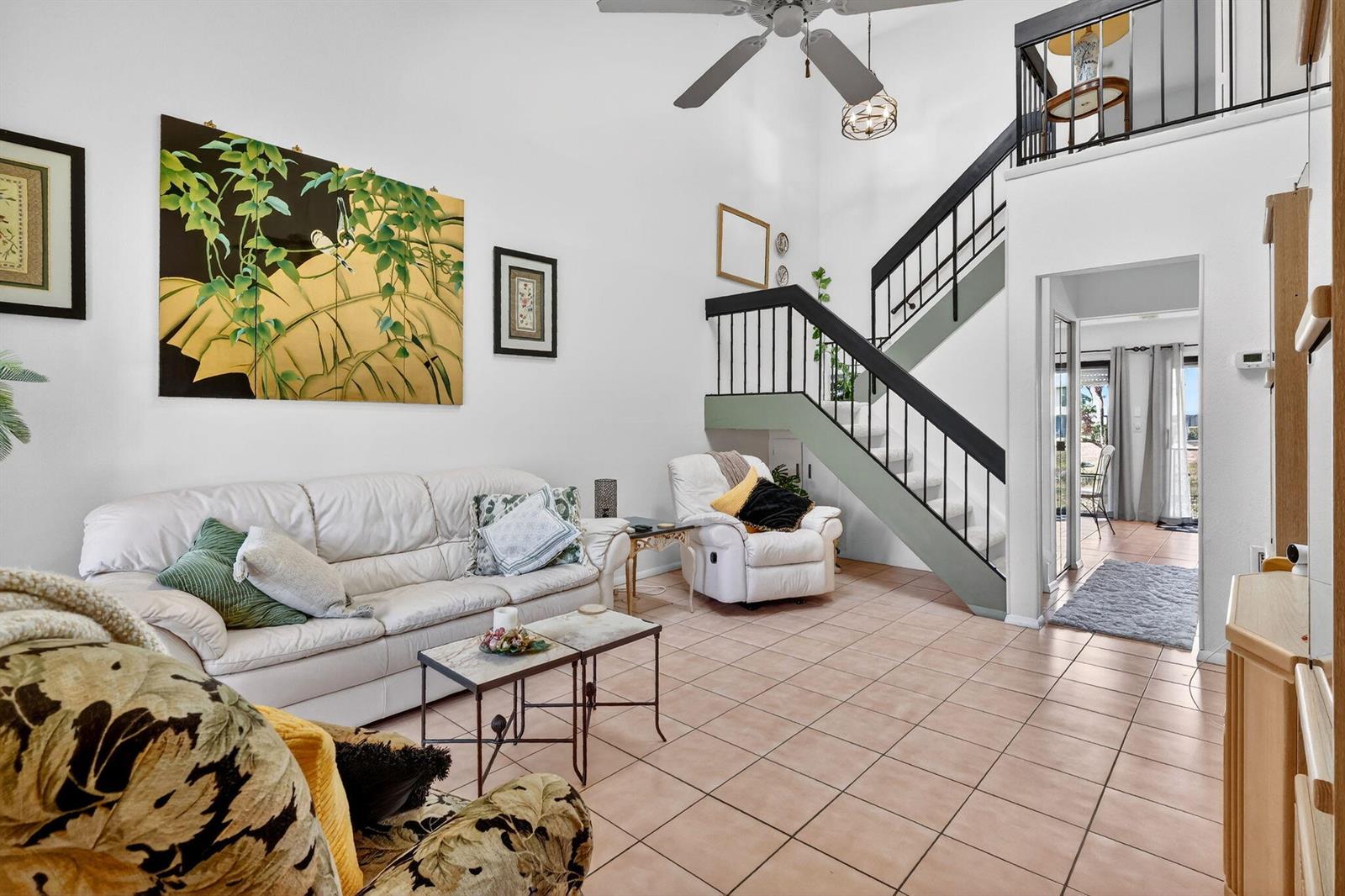 A living room features tile flooring, a white sofa, a staircase, and a large wall painting — PORT ST. LUCIE, FL