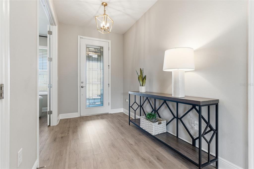 A bright entryway features light wood-look flooring, a geometric console table, and a glass-paneled door — 17674 EVERLONG DRIVE, LAND O LAKES, FL