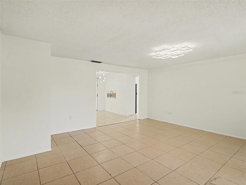 A bright, empty living room features white walls, beige tile flooring, and a modern ceiling light — 4037 MAVERICK AVENUE, SARASOTA, FL