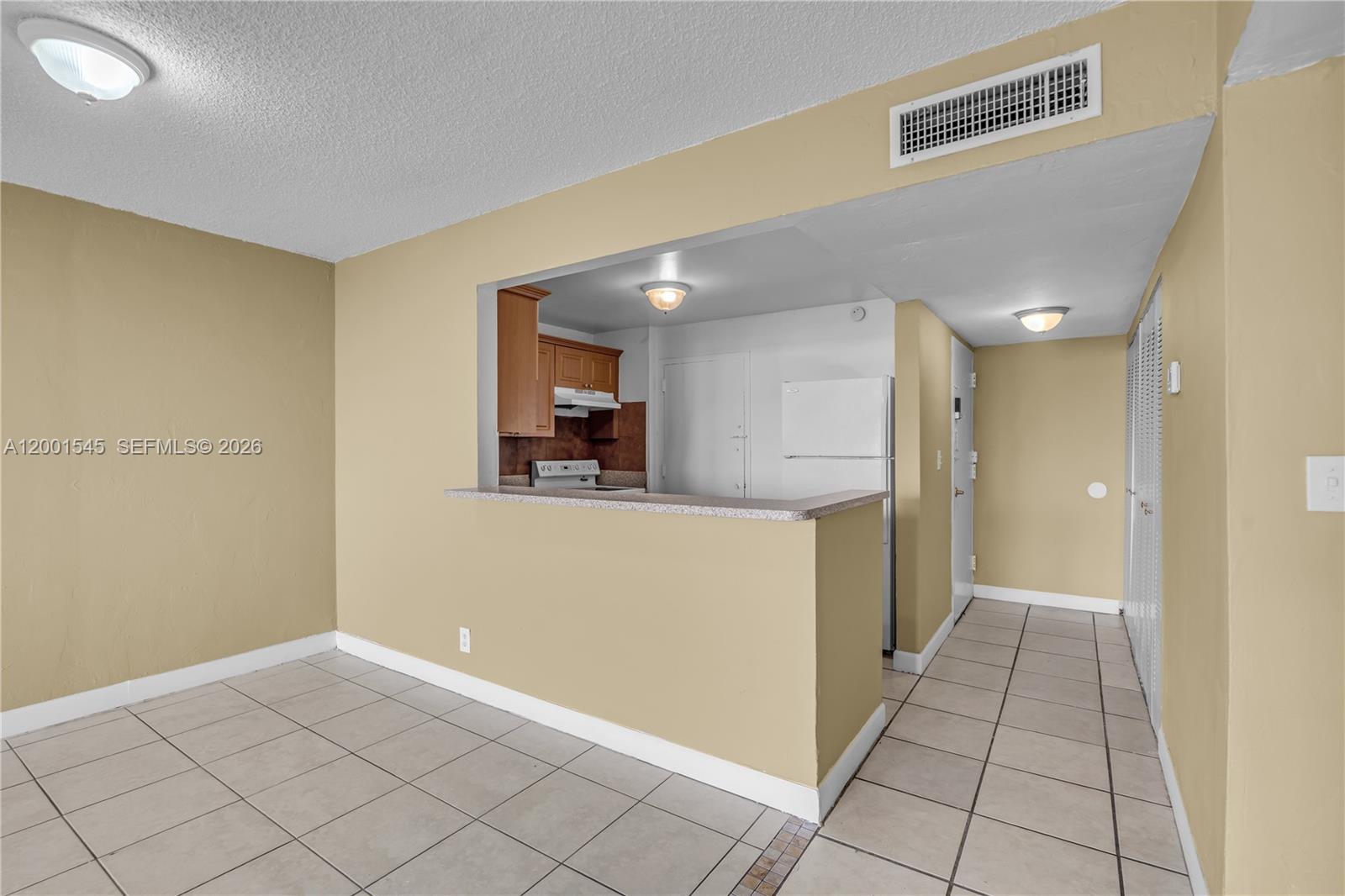 An open kitchen with wood cabinets and white appliances overlooks a tiled dining area — 9143 SW 77th Ave # B802, Miami FL 33156, MIAMI, FL