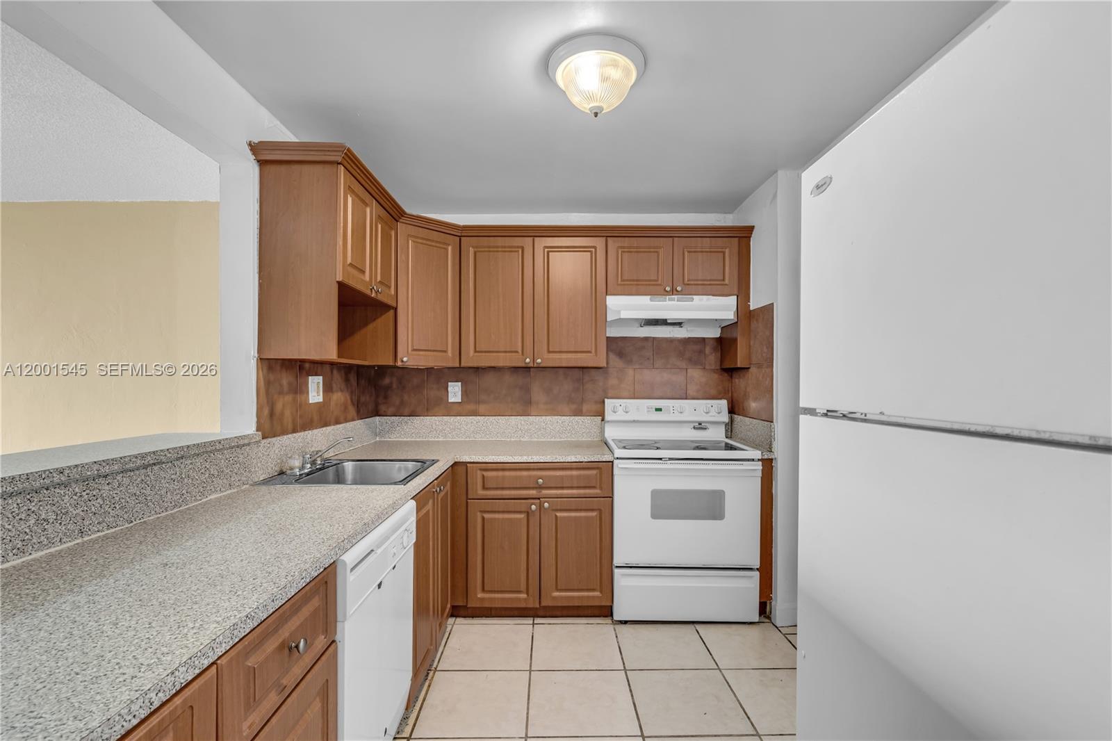 A kitchen features wood cabinets, granite countertops, white appliances, and light-colored tile flooring — 9143 SW 77th Ave # B802, Miami FL 33156, MIAMI, FL