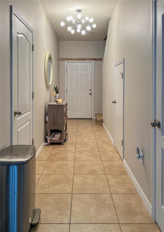 A tiled entryway features a modern chandelier, a wooden console table, and a front door — 772 SPRING FLOWERS TRAIL, BRANDON, FL