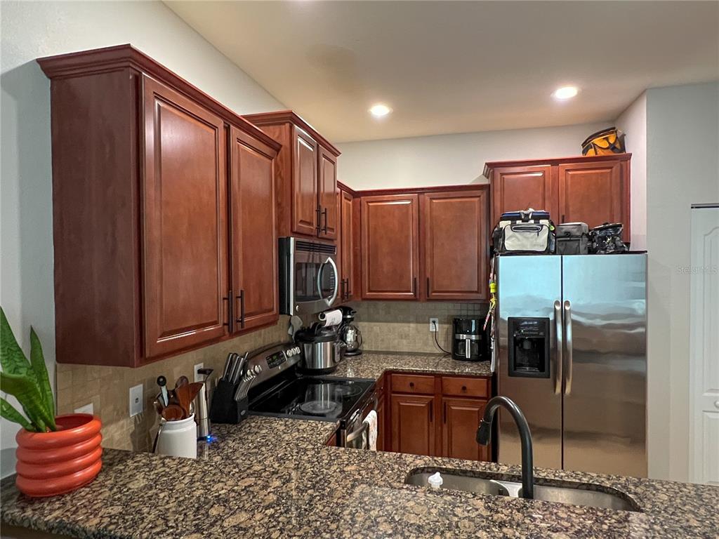 A kitchen features dark wood cabinets, granite countertops, stainless steel appliances, and a tile backsplash — 772 SPRING FLOWERS TRAIL, BRANDON, FL