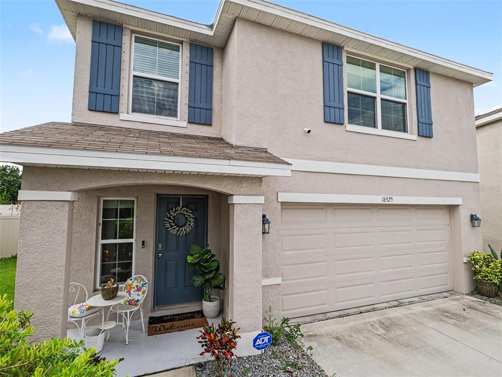 A two-story beige stucco house features a blue front door, shutters, and a two-car garage — 16525 MOSAIC OAR DRIVE, WIMAUMA, FL