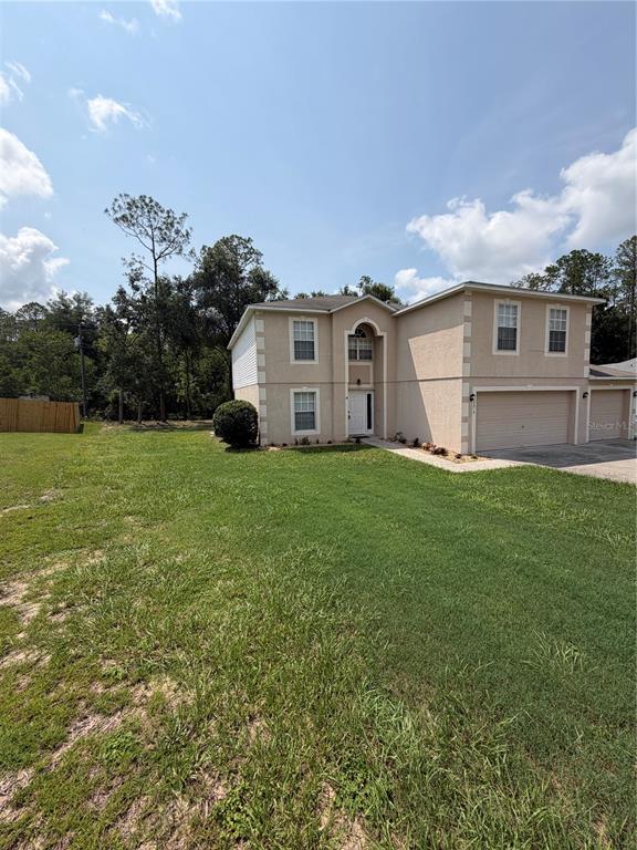 A two-story suburban house with a tan stucco exterior, a three-car garage, and a lawn — 10078 N CARVER WAY, CITRUS SPRINGS, FL