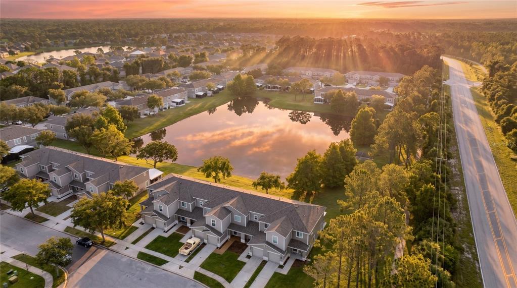 An aerial view shows multi-family townhomes surrounding a central pond at sunset — 2688 SICILY DRIVE, NEW SMYRNA BEACH, FL