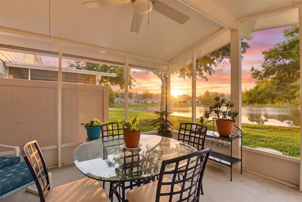 A screened-in patio with a glass table and chairs overlooks a lake at sunset — 2688 SICILY DRIVE, NEW SMYRNA BEACH, FL