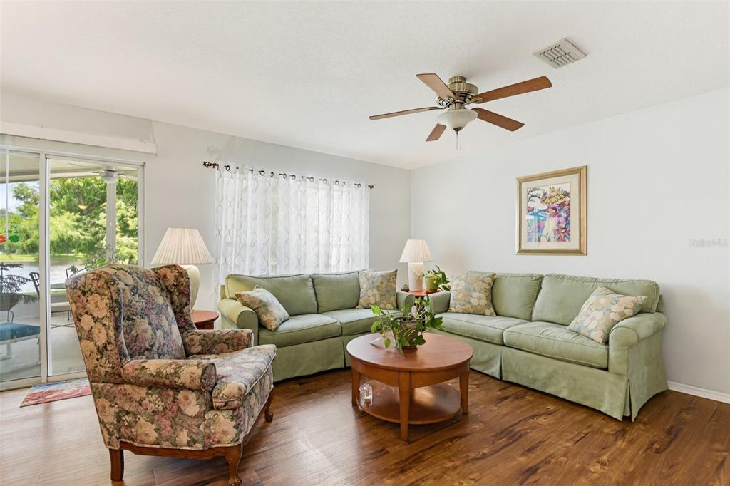 A living room features a green sofa, floral armchair, round wooden coffee table, and wood flooring — 2688 SICILY DRIVE, NEW SMYRNA BEACH, FL