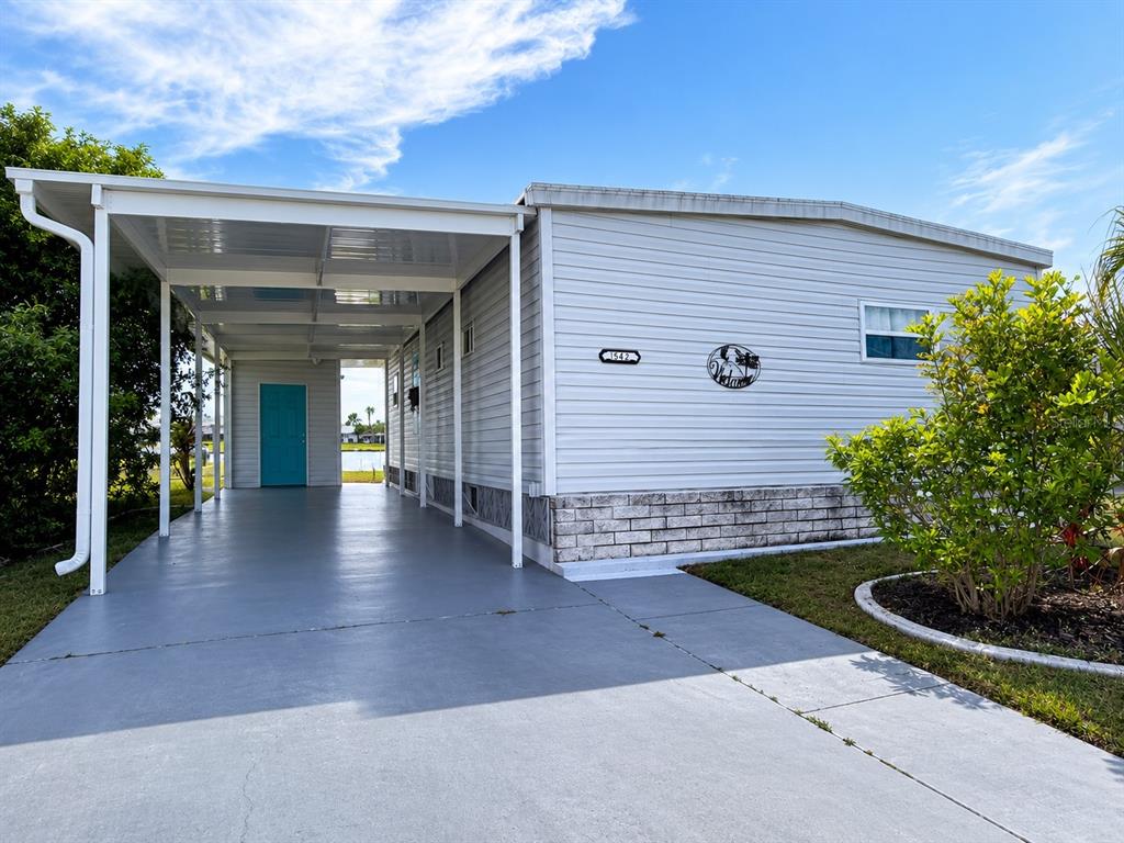 A light-colored mobile home features a long carport and a small front garden area — 542 TAMPICO DRIVE, NORTH PORT, FL