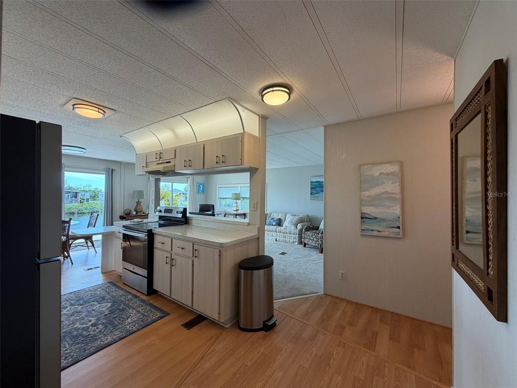 A kitchen with light wood cabinets and a stainless steel stove opens to a living area — 542 TAMPICO DRIVE, NORTH PORT, FL
