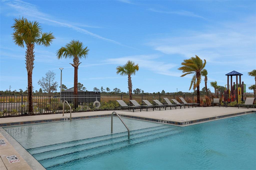 A swimming pool with a shallow entry area, lounge chairs, and palm trees under blue skies — 17030 COTTONTAIL CIRCLE, PUNTA GORDA, FL