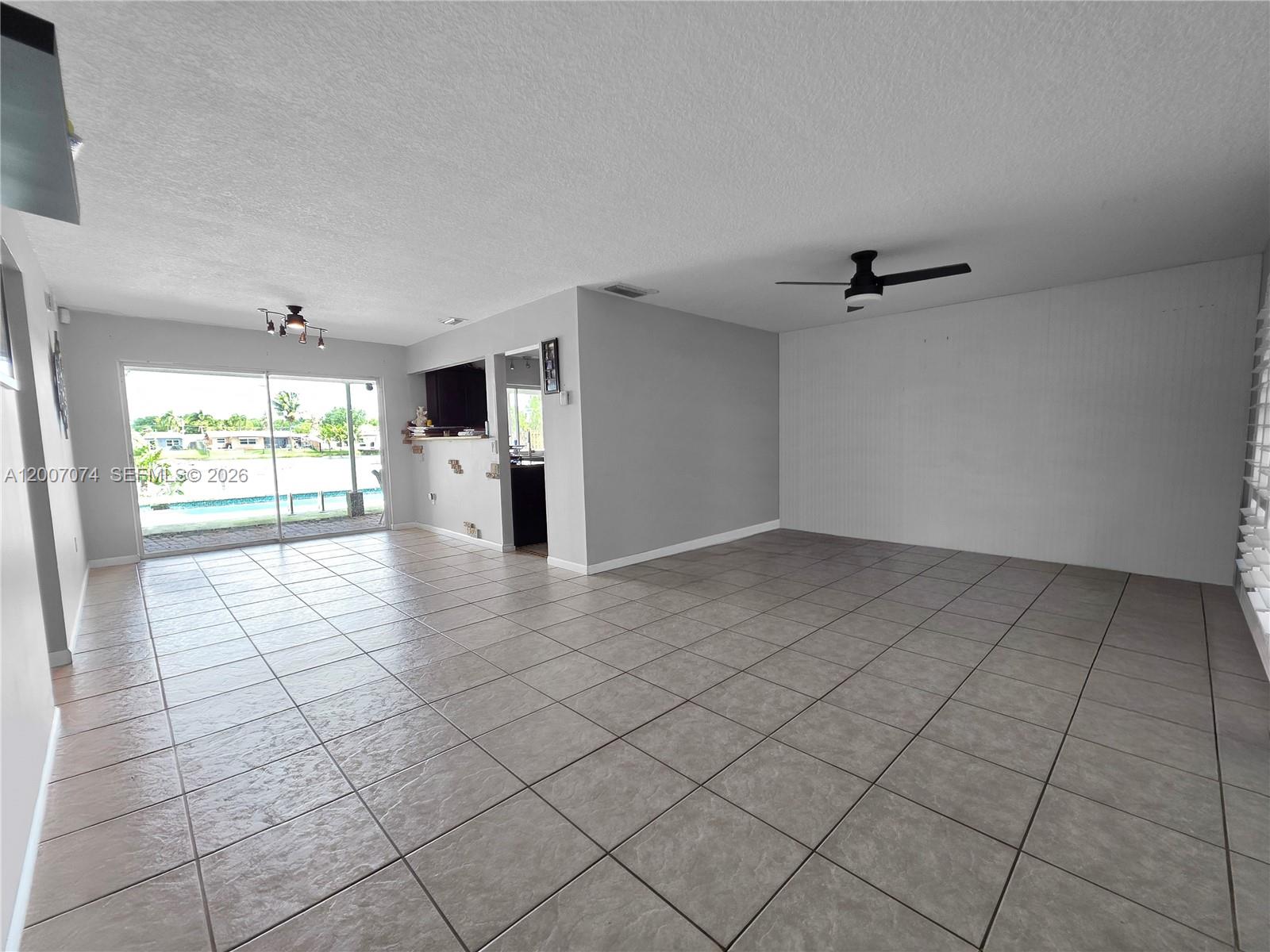 An open living area features large neutral floor tiles, a ceiling fan, and sliding glass doors — 11661 NW 31st Pl, Sunrise FL 33323, SUNRISE, FL