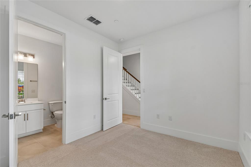 A carpeted bedroom features a white door, a doorway to a bathroom, and a staircase — 234 PASQUALA WAY, OVIEDO, FL