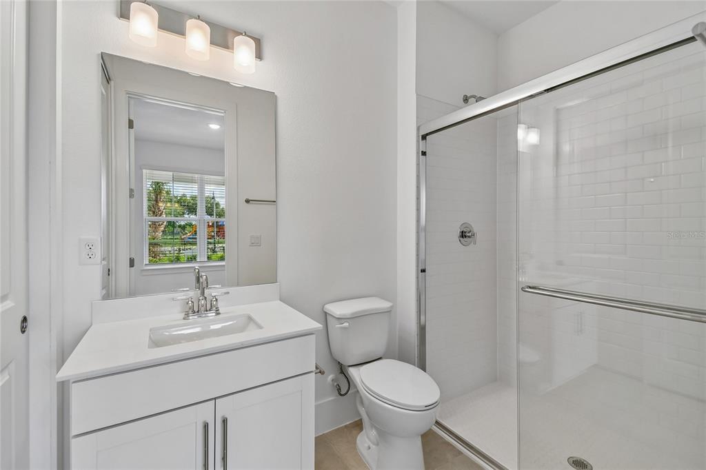 A bathroom features a white vanity, a toilet, and a glass-enclosed shower with subway tiles — 234 PASQUALA WAY, OVIEDO, FL
