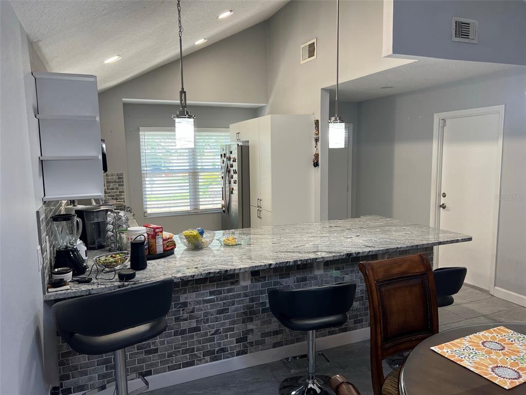 A kitchen features a granite breakfast bar, gray tiled base, and two pendant lights — 3159 BERRIDGE LANE, ORLANDO, FL