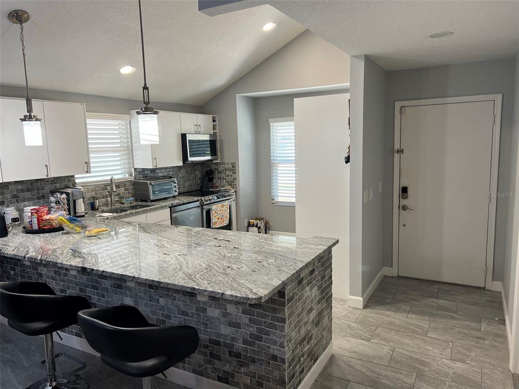 A kitchen features a granite breakfast bar, gray tiled backsplash, white cabinets, and stainless appliances — 3159 BERRIDGE LANE, ORLANDO, FL
