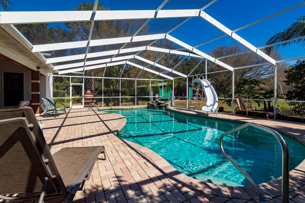 A swimming pool with a slide and waterfall sits inside a screened-in patio enclosure — 9215 RIDGE ROAD, NEW PORT RICHEY, FL