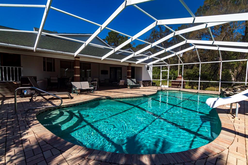 A swimming pool with a white screen enclosure sits on a brick patio behind a house — 9215 RIDGE ROAD, NEW PORT RICHEY, FL