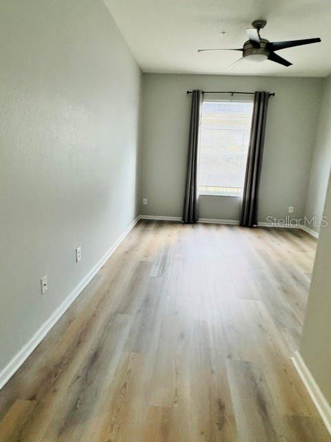 An empty room features light gray walls, wood-look flooring, a ceiling fan, and a window — 7135 YACHT BASIN AVENUE UNIT 239, ORLANDO, FL