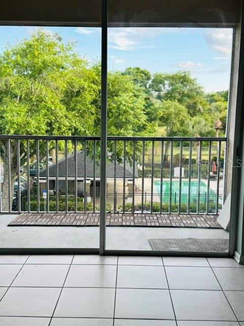 A tiled balcony overlooks a swimming pool and trees through a large sliding glass door — 7135 YACHT BASIN AVENUE UNIT 239, ORLANDO, FL