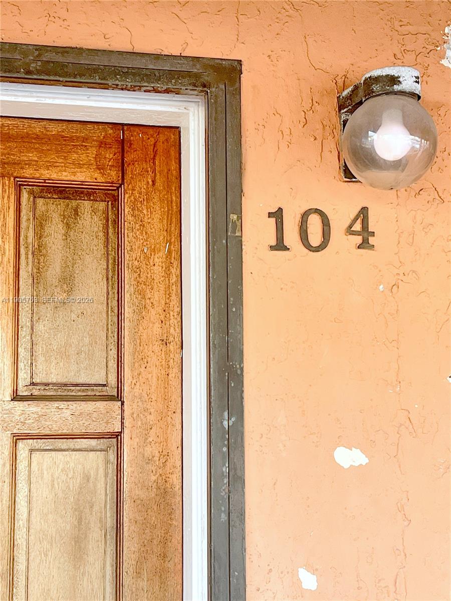 A wooden door sits next to a wall with the number 104 and a light fixture — 2740 W 63rd St # 104, Hialeah FL 33016, HIALEAH, FL