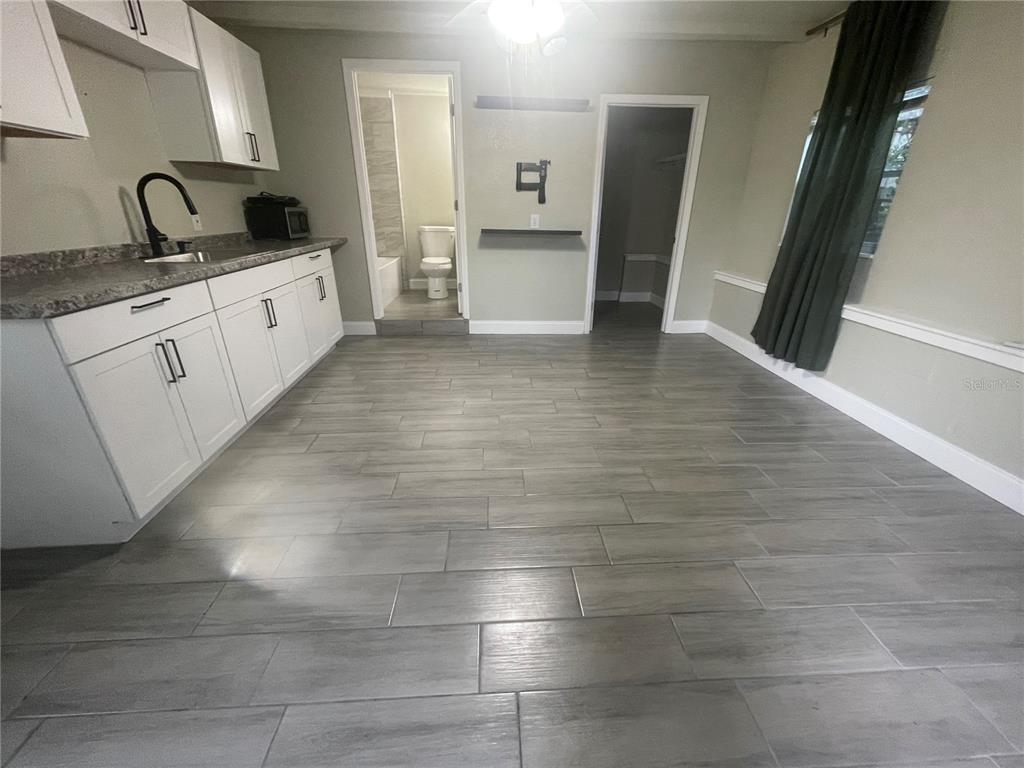 A kitchen with white cabinets, gray wood-look tile flooring, and an adjacent bathroom — 3419 19TH STREET E UNIT Back ADU, BRADENTON, FL