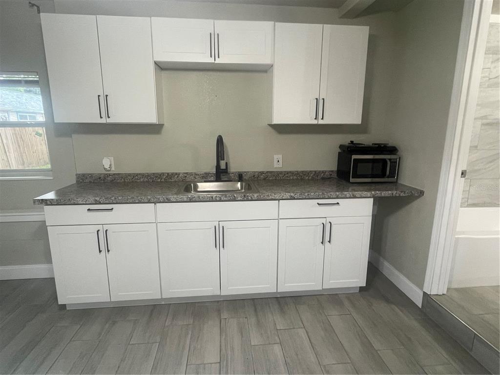 A kitchen features white cabinets, a gray speckled countertop, a sink, and a microwave — 3419 19TH STREET E UNIT Back ADU, BRADENTON, FL