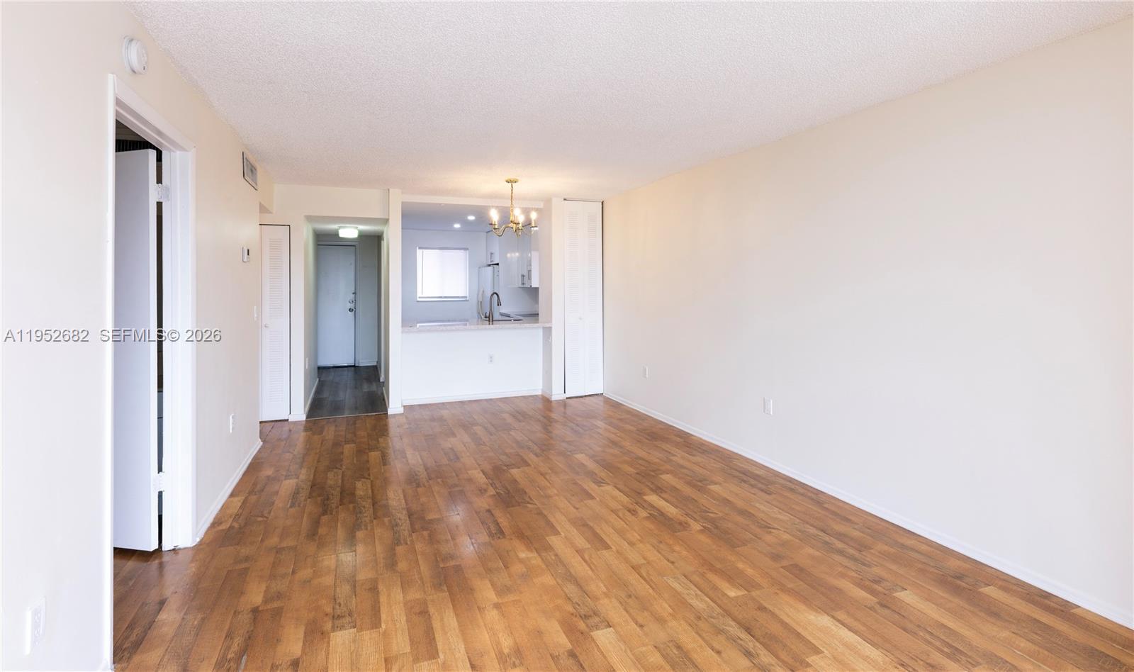 An empty living room features wood-look flooring, white walls, and an open kitchen pass-through — 19701 SW 114th Ave # 364, Miami FL 33157, MIAMI, FL