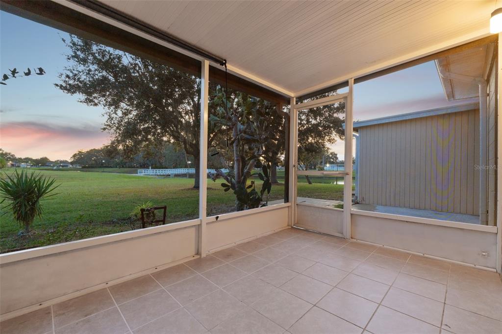 A tiled screened-in porch overlooks a grassy yard with trees and a small pond — 3515 CLUB CIRCLE, LAKESHORE, FL