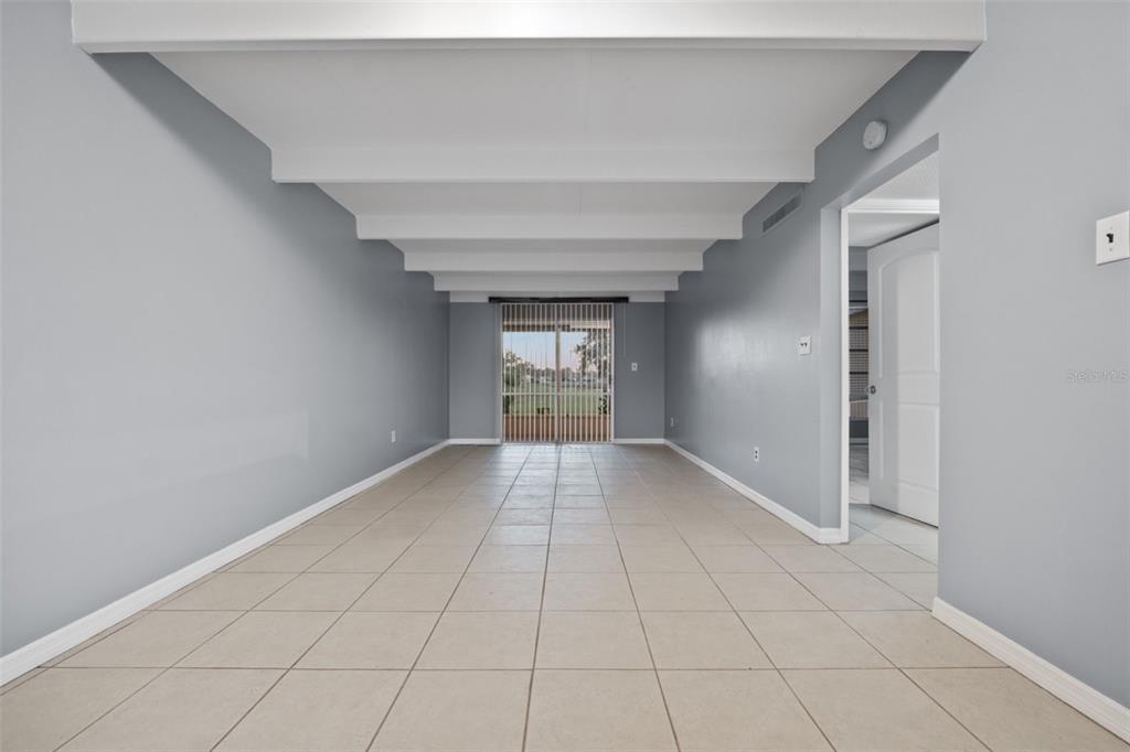 An empty room features light gray walls, a tiled floor, and exposed white ceiling beams — 3515 CLUB CIRCLE, LAKESHORE, FL