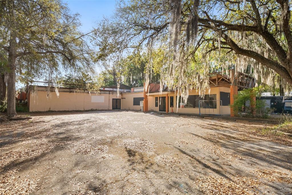 A single-story commercial building with a large paved parking lot under moss-draped oak trees — 519 NW 10TH AVENUE, GAINESVILLE, FL