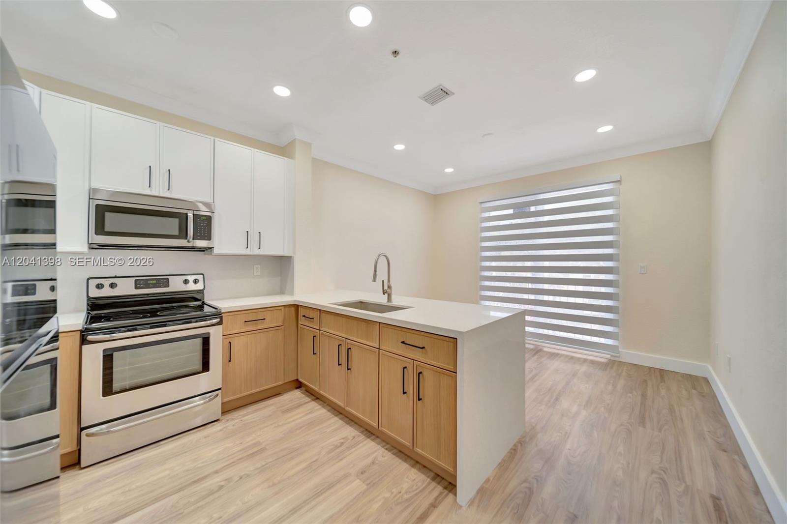 A modern kitchen features white upper cabinets, light wood lower cabinets, and a quartz island — 17620 NW 73rd Ave # 17, Hialeah FL 33015, HIALEAH, FL