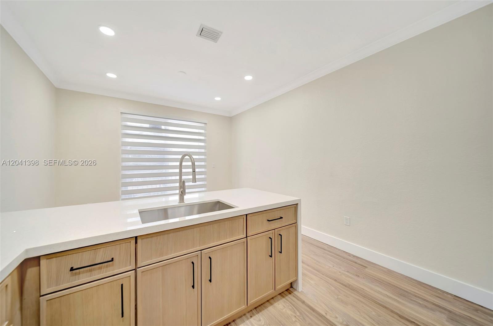 A kitchen island with a stainless steel sink and light wood cabinets sits in a room — 17620 NW 73rd Ave # 17, Hialeah FL 33015, HIALEAH, FL