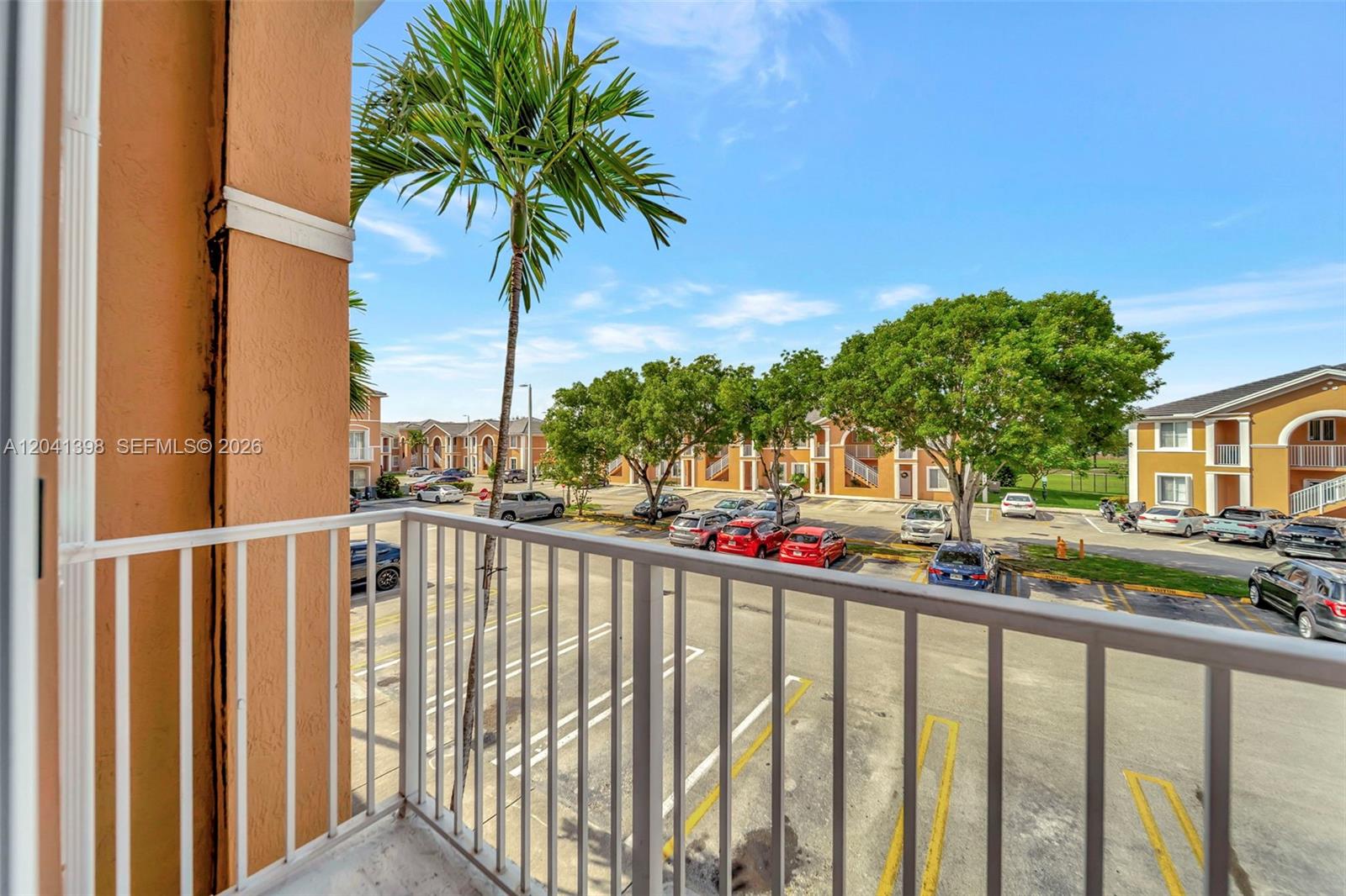A view from a balcony overlooking a parking lot and apartment buildings with palm trees — 17620 NW 73rd Ave # 17, Hialeah FL 33015, HIALEAH, FL