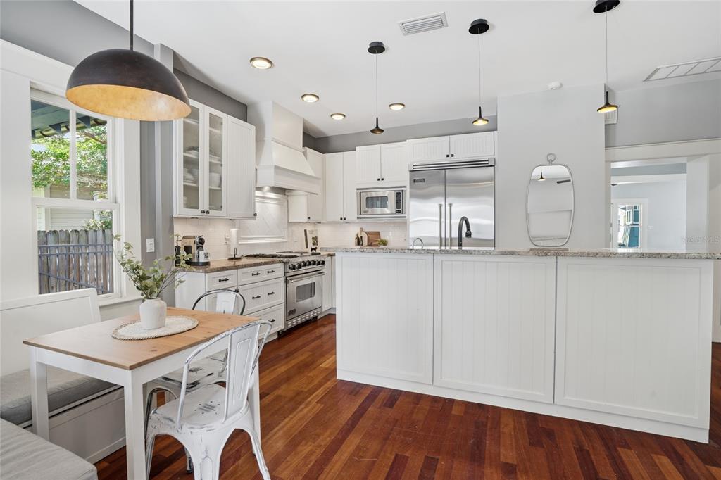 A kitchen features white cabinetry, stainless steel appliances, a breakfast nook, and hardwood flooring — 2116 W WATROUS AVENUE, TAMPA, FL