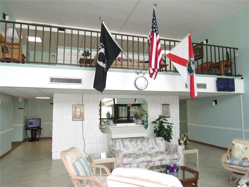 A lobby area features a lofted balcony, three flags, a white brick wall, and seating — 21260 BRINSON AVENUE UNIT 212, PORT CHARLOTTE, FL