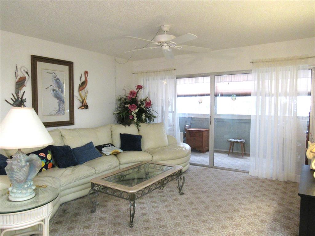A living room features a white sectional sofa, glass coffee table, and sliding glass balcony doors — 21260 BRINSON AVENUE UNIT 212, PORT CHARLOTTE, FL