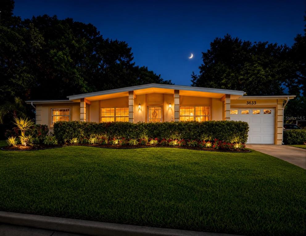 A single-story house with a lit front yard, landscaping, and a garage at twilight — 3633 RANCHWOOD ROAD, ORLANDO, FL