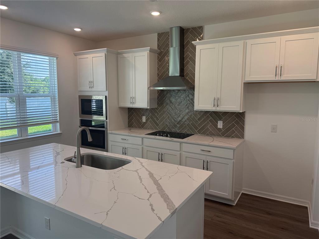 A modern kitchen features white cabinets, a herringbone tile backsplash, and a marble-patterned island countertop — 2692 CAVANAUGH DRIVE, ORLANDO, FL