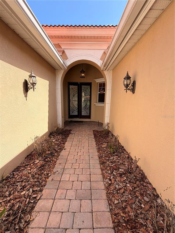 A brick walkway leads to a front door framed by an arched entryway and wall sconces — 11316 RAPALLO LANE, WINDERMERE, FL