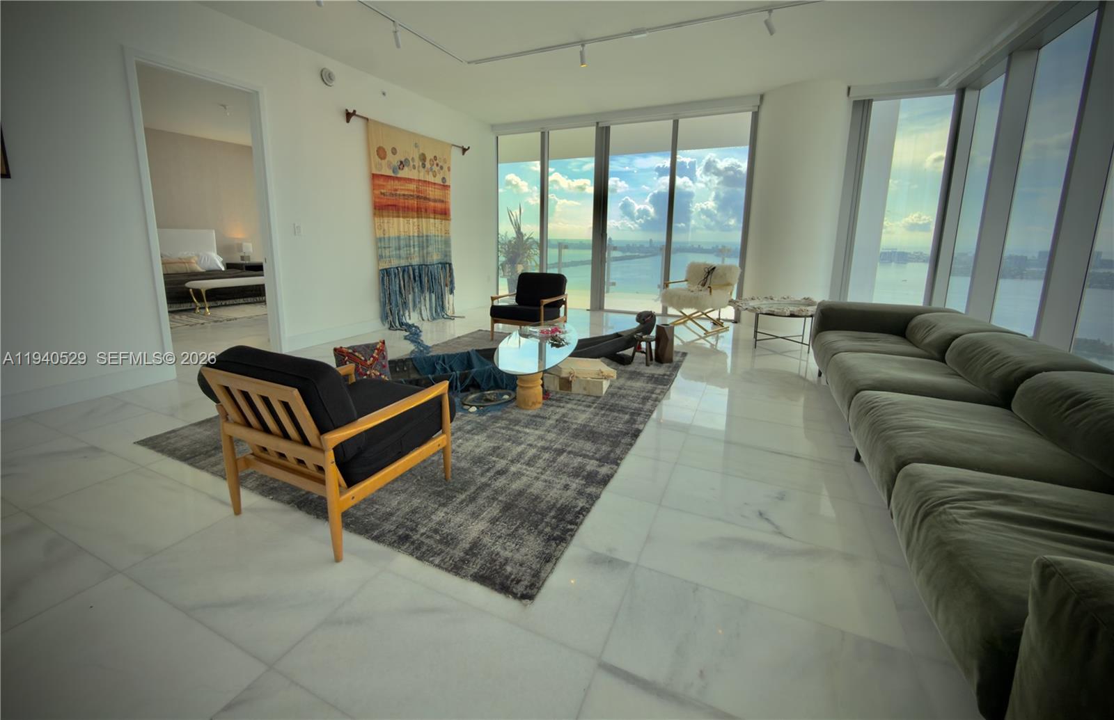 A modern living room features marble floors, floor-to-ceiling windows, and a view of the water — 700 NE 26th Terrace # 4403, Miami FL 33137, MIAMI, FL