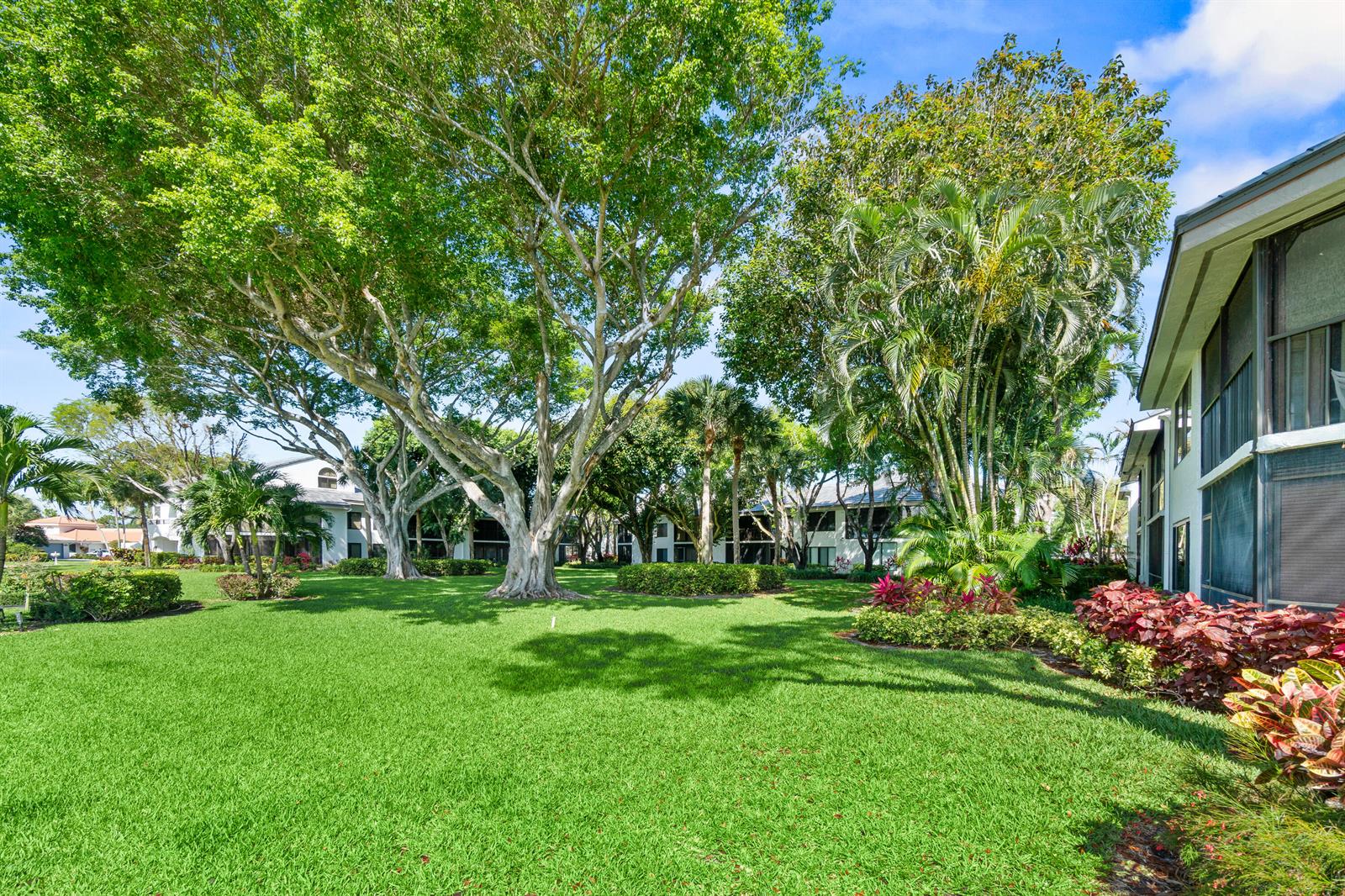 A grassy courtyard with large trees and tropical landscaping sits between two multi-story residential buildings — 7533 Glendevon Lane # 905, Delray Beach FL 33446, DELRAY BEACH, FL
