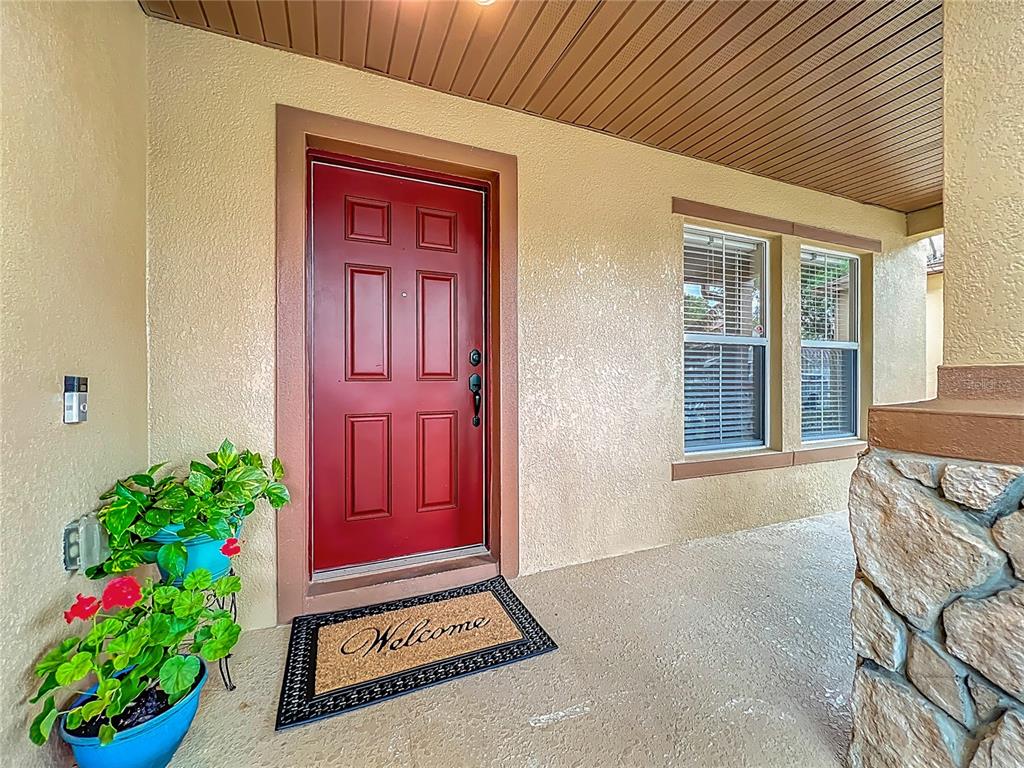 A red front door with a welcome mat sits on a covered porch with stone — 14932 PERDIDO DRIVE, ORLANDO, FL