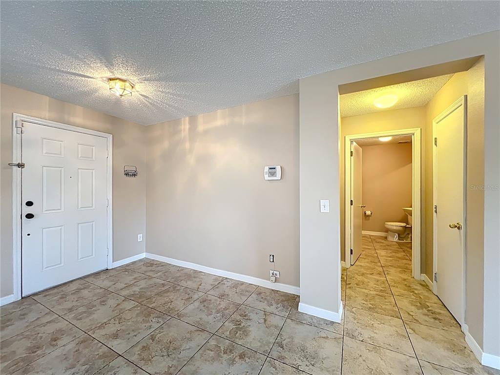 A room with tiled flooring, a white front door, and an open doorway to a bathroom — 14932 PERDIDO DRIVE, ORLANDO, FL