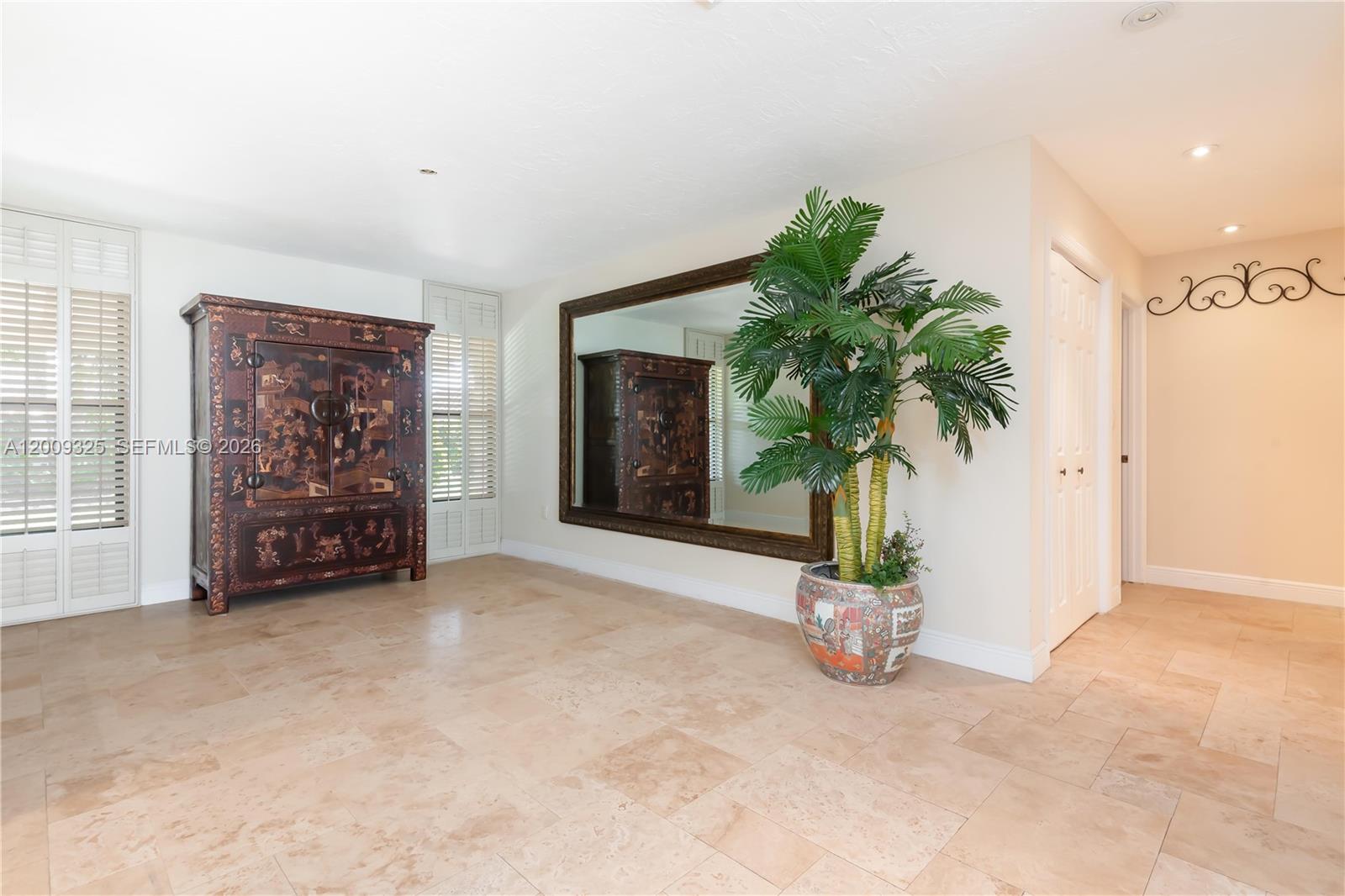 A room with beige tile flooring, a large wall mirror, an ornate cabinet, and a potted palm — 13300 SW 21st St, Miami FL 33175, MIAMI, FL