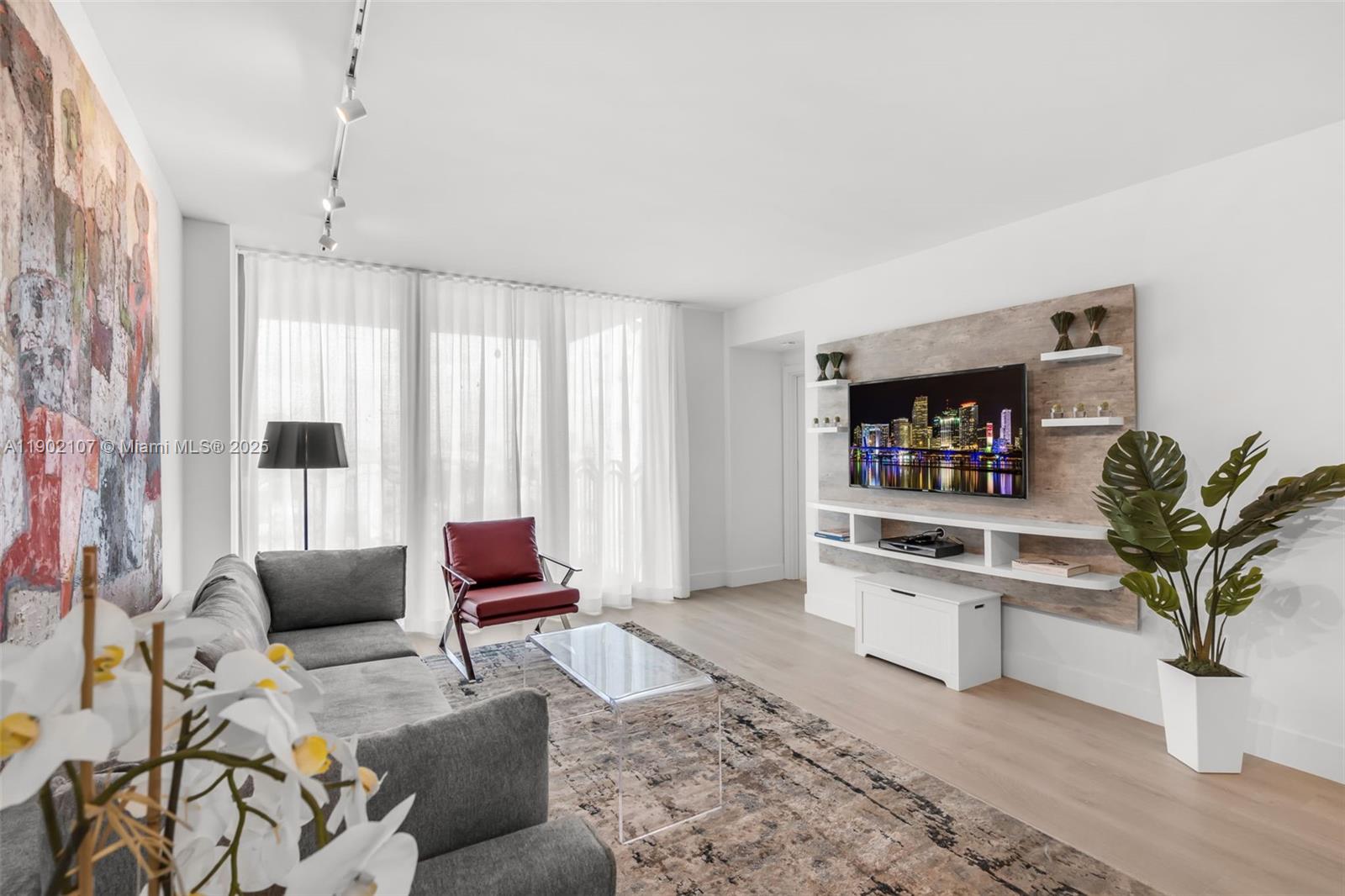 A modern living room features a grey sofa, red armchair, and a wall-mounted television — 1500 Ocean Dr # 1109, Miami Beach FL 33139, MIAMI BEACH, FL