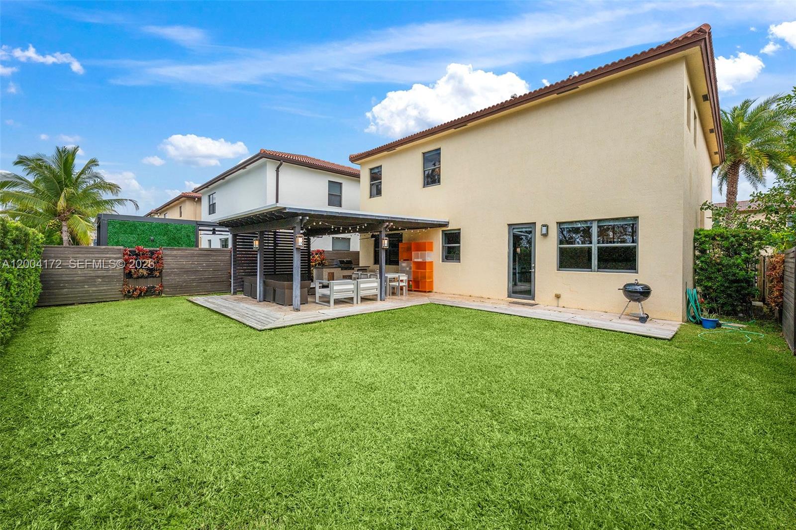 A backyard features a wooden deck with a pergola, outdoor furniture, and a grassy lawn — 9890 NW 86th Ter, Doral FL 33178, DORAL, FL